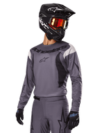 Alpinestars 2025 Fluid Haul Gear Set, grijs motorcross shirt en broek met zwarte en witte accenten, gedragen met een zwarte helm, rode crossbril en zwarte handschoenen, sportieve pasvorm voor off-road rijden