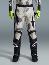 Alpinestars 2026 Racer Lahnd Pants, motorcrossbroek, Sand Camo-patroon met grijze en paarse abstracte graphics, gedragen met neongele handschoenen en zwarte laarzen, voorzien van zwarte sterlogo's op de dijen en een zwarte tailleriem, duurzame off-road race-uitrusting