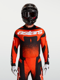 Alpinestars Techstar Swan jersey, heren motorcrossjersey in cardinalrood en zwart, atletische racepasvorm, ademend stretchmateriaal, gedragen door model met helm en MX-uitrusting.