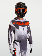 Alpinestars Techstar Swan Jersey, motocross jersey voor heren, grijs en rood fluo, gedragen door model met helm en handschoenen, atletische racepasvorm.