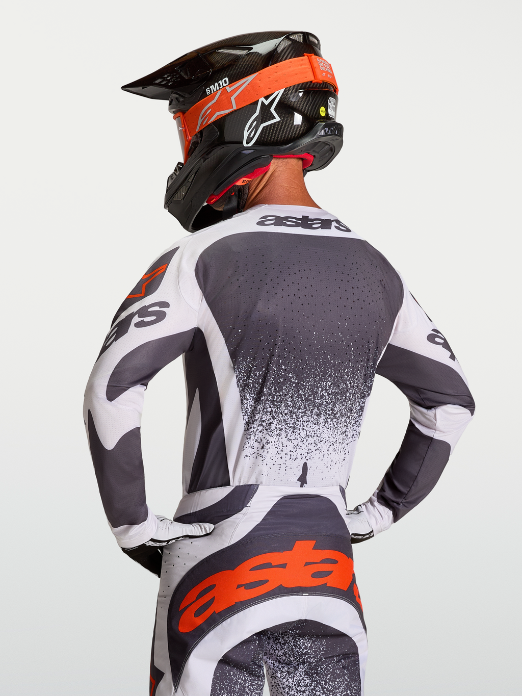 Alpinestars Techstar Swan Jersey, atletische motorcrossjersey voor heren in donkergrijs en wit met rode accenten, getoond vanaf de rugzijde op een rijder met helm.