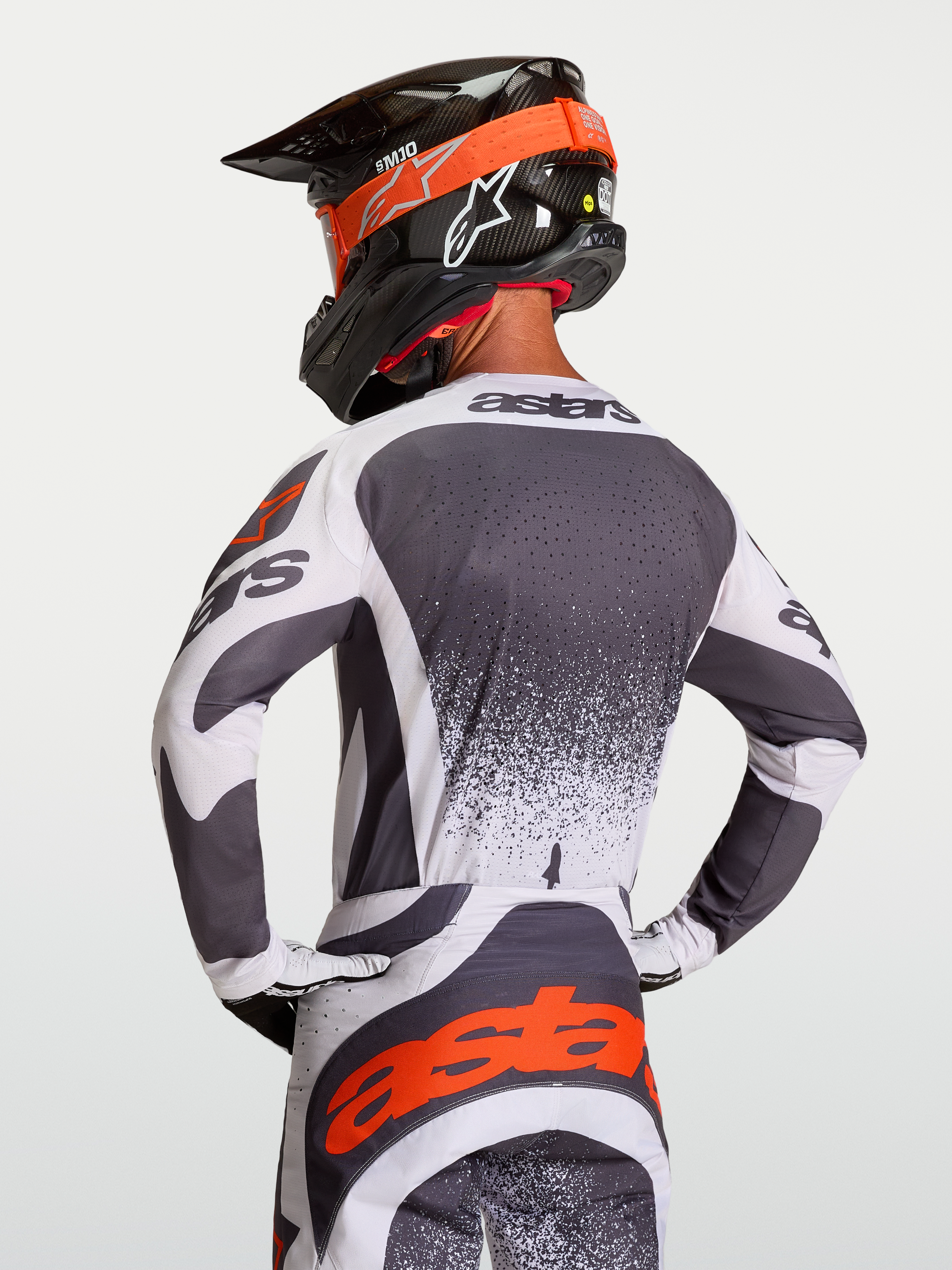 Alpinestars Techstar Swan Jersey, atletische motorcrossjersey voor heren in donkergrijs en wit met rode accenten, getoond vanaf de rugzijde op een rijder met helm.