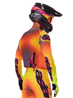 Alpinestars 2025 Supertech Lipan Gear Set, motorcrosser van achteren en opzij gezien, geel, oranje en rood kleurverloop met zwarte en roze branding, zwarte helm met roze accenten en oranje bril, professionele off-road race-uitrusting