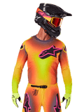 Motocrossrijder in de 2025 Supertech Lipan Jersey, levendig geel, oranje en roze kleurverloop, groot zwart Alpinestars sterlogo met roze omtrek op de borst, lasergesneden perforaties voor ventilatie, atletische racepasvorm, gecombineerd met bijpassende broek, gele handschoenen en een zwarte helm met crossbril.