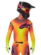 Motocrossrijder in de 2025 Supertech Lipan Jersey, levendig geel, oranje en roze kleurverloop, groot zwart Alpinestars sterlogo met roze omtrek op de borst, lasergesneden perforaties voor ventilatie, atletische racepasvorm, gecombineerd met bijpassende broek, gele handschoenen en een zwarte helm met crossbril.
