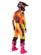 Alpinestars 2025 Supertech Lipan Gear Set, motorcrosser van achteren gezien, geel en oranje jersey met kleurverloop en roze accenten, bijpassende broek, felroze laarzen en zwarte helm met roze en gele graphics, professionele race-outfit