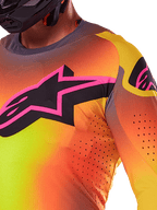 Close-up van de Alpinestars 2025 Supertech Lipan Jersey in Yellow Pink, met een levendig kleurverloop, een groot zwart sterlogo met een roze rand op de borst en zichtbare lasergesneden perforaties voor een verbeterde luchtstroom.