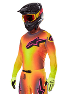 Motocrossrijder in de Alpinestars 2025 Supertech Lipan Gear Set, met een geel en oranje kleurverloop jersey met een roze en zwart Astars-logo, neongele handschoenen en een zwarte helm met rode crossbril, professionele off-road race-uitrusting.