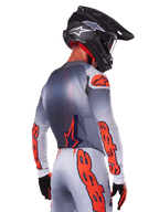 Motocrossrijder van achteren die de Alpinestars 2025 Supertech Lipan Jersey in Gray Orange Fluo draagt, met opvallende oranje logo's op de mouwen en rug, gecombineerd met een bijpassende broek en een zwarte helm, professionele race-outfit voor off-road prestaties.