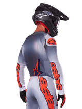 Motocrossrijder van achteren die de Alpinestars 2025 Supertech Lipan Jersey in Gray Orange Fluo draagt, met opvallende oranje logo's op de mouwen en rug, gecombineerd met een bijpassende broek en een zwarte helm, professionele race-outfit voor off-road prestaties.