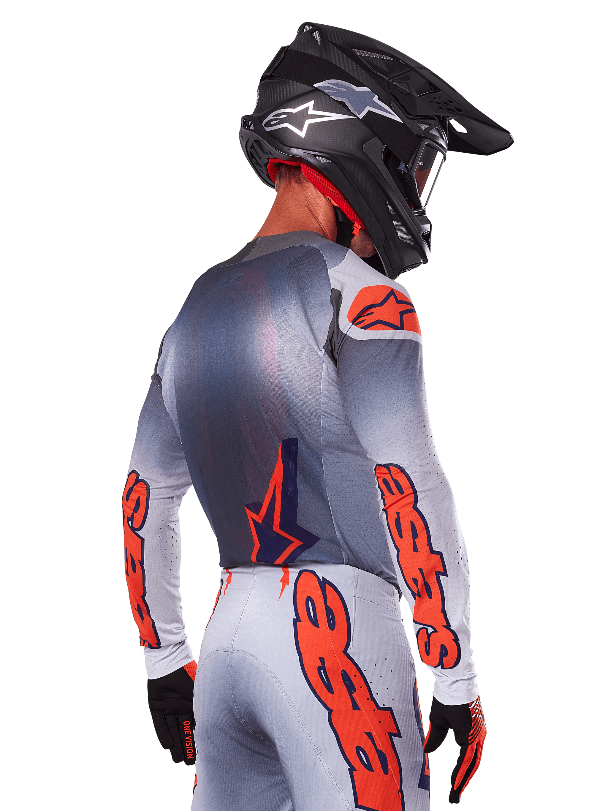 Motocrossrijder van achteren die de Alpinestars 2025 Supertech Lipan Jersey in Gray Orange Fluo draagt, met opvallende oranje logo's op de mouwen en rug, gecombineerd met een bijpassende broek en een zwarte helm, professionele race-outfit voor off-road prestaties.