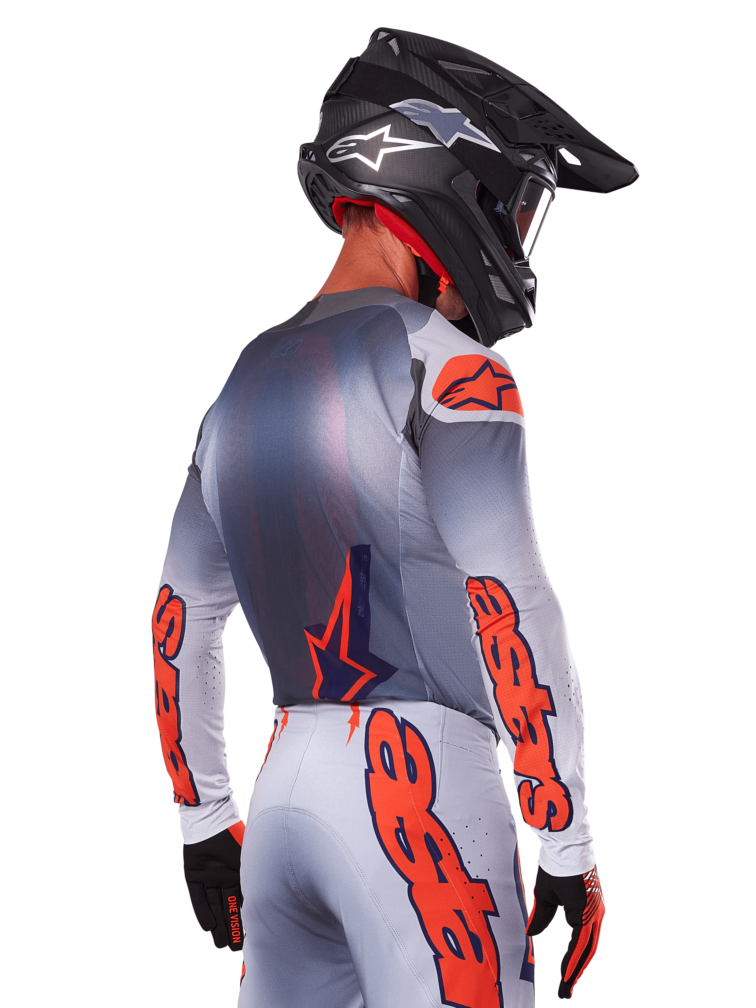 Motocrossrijder van achteren die de Alpinestars 2025 Supertech Lipan Jersey in Gray Orange Fluo draagt, met opvallende oranje logo's op de mouwen en rug, gecombineerd met een bijpassende broek en een zwarte helm, professionele race-outfit voor off-road prestaties.