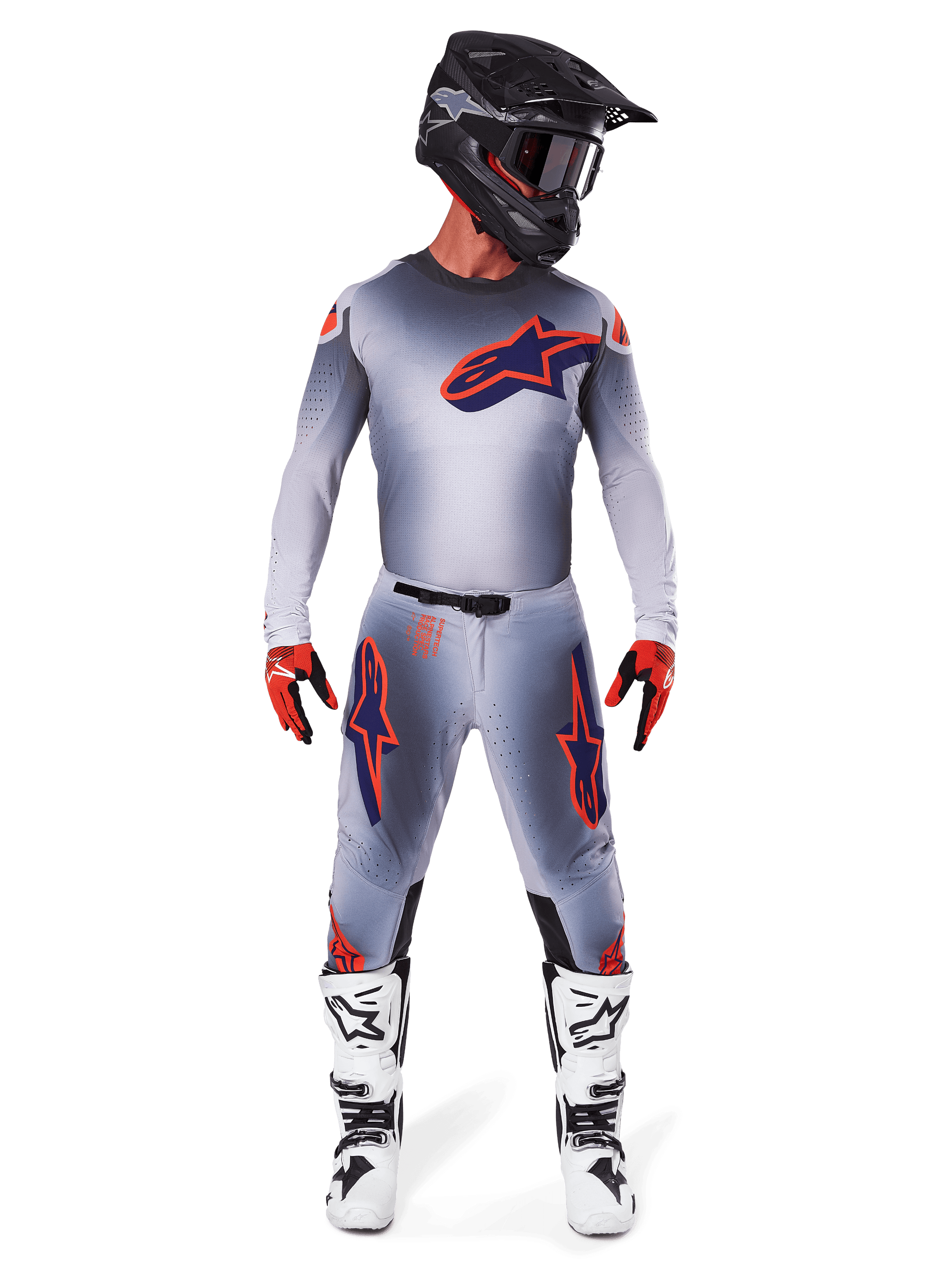 Motorcrosser die het Alpinestars 2025 Supertech Lipan Jersey in Gray Orange Fluo draagt, voorzien van een grijs kleurverloop en oranje logo, gecombineerd met een bijpassende motorcrossbroek, zwarte helm, witte laarzen en oranje handschoenen, gecoördineerde professionele race-uitrusting.