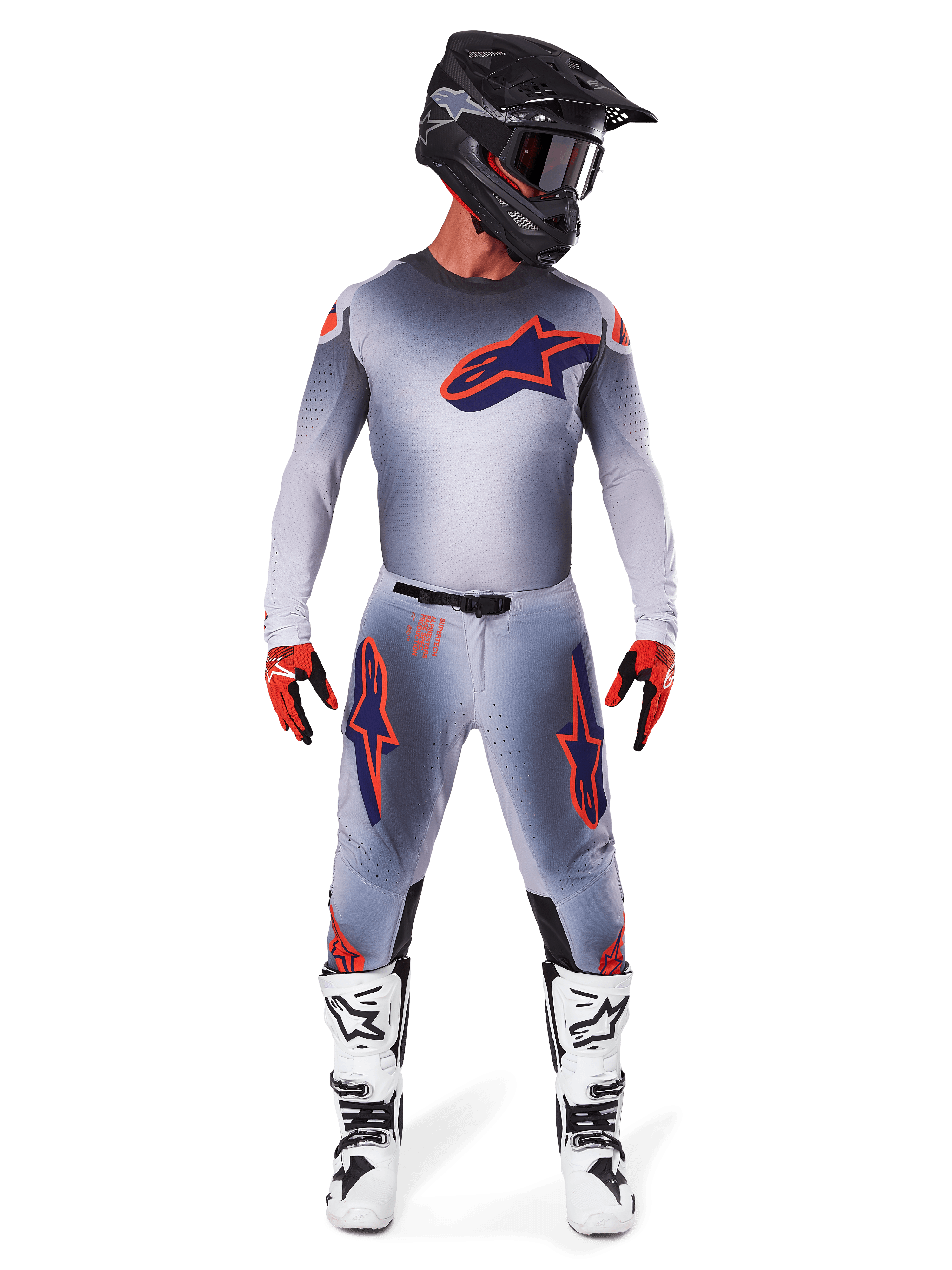 Motorcrosser die het Alpinestars 2025 Supertech Lipan Jersey in Gray Orange Fluo draagt, voorzien van een grijs kleurverloop en oranje logo, gecombineerd met een bijpassende motorcrossbroek, zwarte helm, witte laarzen en oranje handschoenen, gecoördineerde professionele race-uitrusting.