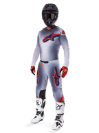 Motorcrosser die de Alpinestars 2025 Supertech Lipan Jersey draagt in grijs en oranje fluo, bijpassende grijze broek met oranje accenten, zwarte helm, witte en zwarte laarzen en oranje-zwarte handschoenen, professionele uitrustingset voor off-road racing.