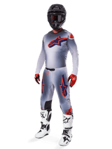 Motorcrosser die de Alpinestars 2025 Supertech Lipan Jersey draagt in grijs en oranje fluo, bijpassende grijze broek met oranje accenten, zwarte helm, witte en zwarte laarzen en oranje-zwarte handschoenen, professionele uitrustingset voor off-road racing.