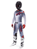 Alpinestars 2025 Supertech Lipan Gear Set, motorcross race-uitrusting, grijs met fluo oranje en marineblauwe ster-graphics, gedragen met een zwarte helm, rood-zwarte handschoenen en wit-zwarte laarzen, complete professionele off-road outfit met geventileerd ontwerp