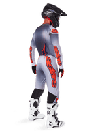 Alpinestars 2025 Supertech Lipan Gear Set, motocrossrijder van achteren gezien, grijs en oranje fluo jersey met bijpassende broek, opvallende oranje branding op de mouwen en pijpen, zwarte helm, wit-zwarte motorcrosslaarzen, professionele off-road race-outfit