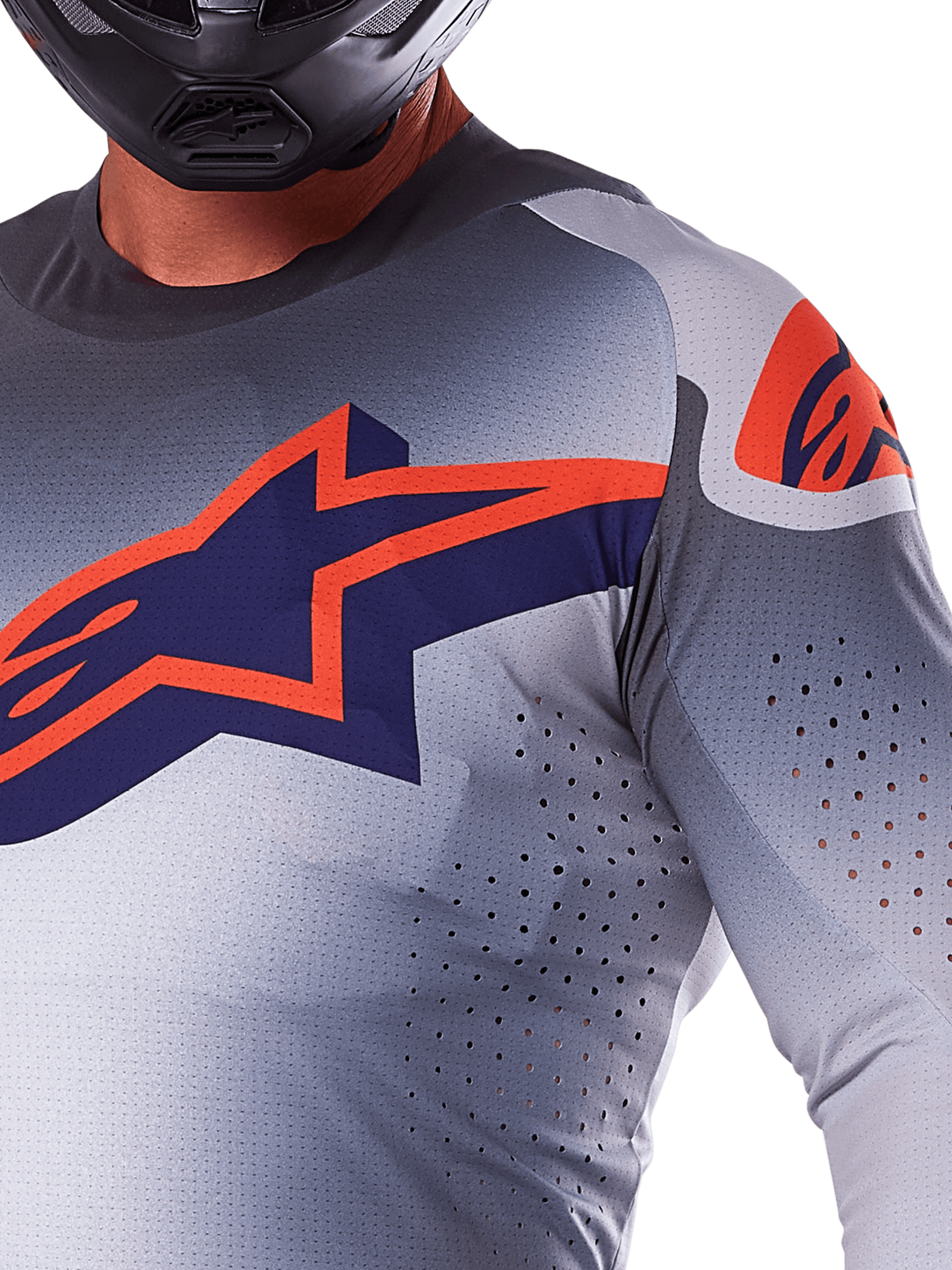 Close-up van een rijder die de Alpinestars 2025 Supertech Lipan Jersey draagt, motorcross jersey, grijs en fluo oranje, voorzien van een groot oranje Alpinestars-logo op de borst, lasergesneden ventilatieopeningen en een zwarte helm, professionele race-uitrusting.