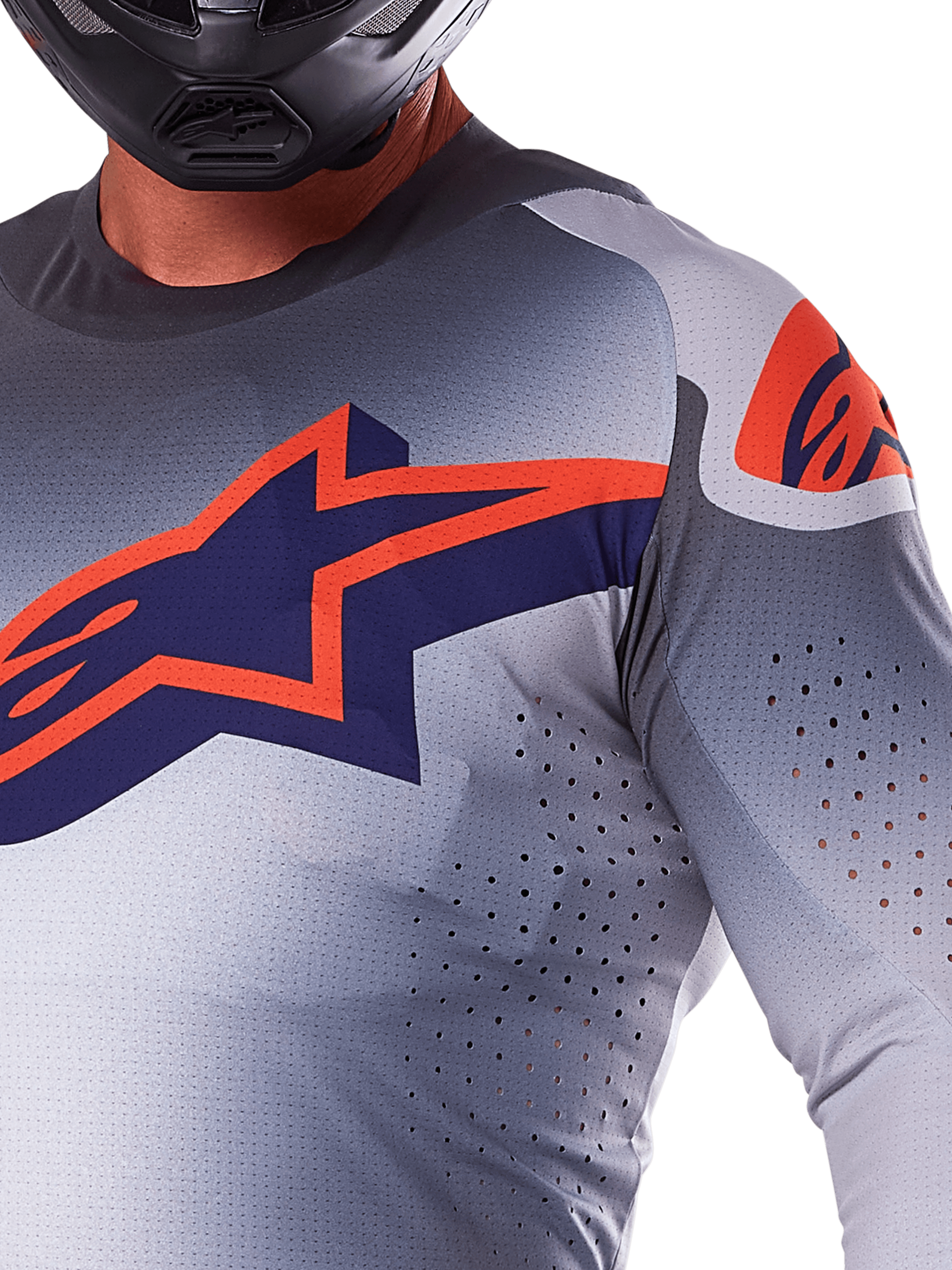 Close-up van een rijder die de Alpinestars 2025 Supertech Lipan Jersey draagt, motorcross jersey, grijs en fluo oranje, voorzien van een groot oranje Alpinestars-logo op de borst, lasergesneden ventilatieopeningen en een zwarte helm, professionele race-uitrusting.