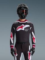 Alpinestars 2026 Supertech AFD Vista Jersey, motorcross shirt in zwart, rood en wit, getoond op een rijder met een zwarte helm, crossbril en handschoenen, voorzien van een groot logo op de borst en 'SUPERTECH AFD' branding, professionele racekleding voor off-road prestaties