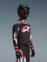 Motocrossrijder in de Alpinestars 2026 Supertech AFD Vista Jersey in zwart, rood en wit, met een groot rood sterlogo op de borst en laser-gesneden perforaties, gecombineerd met een zwarte helm en bijpassende motorcrossbroek voor off-road prestaties