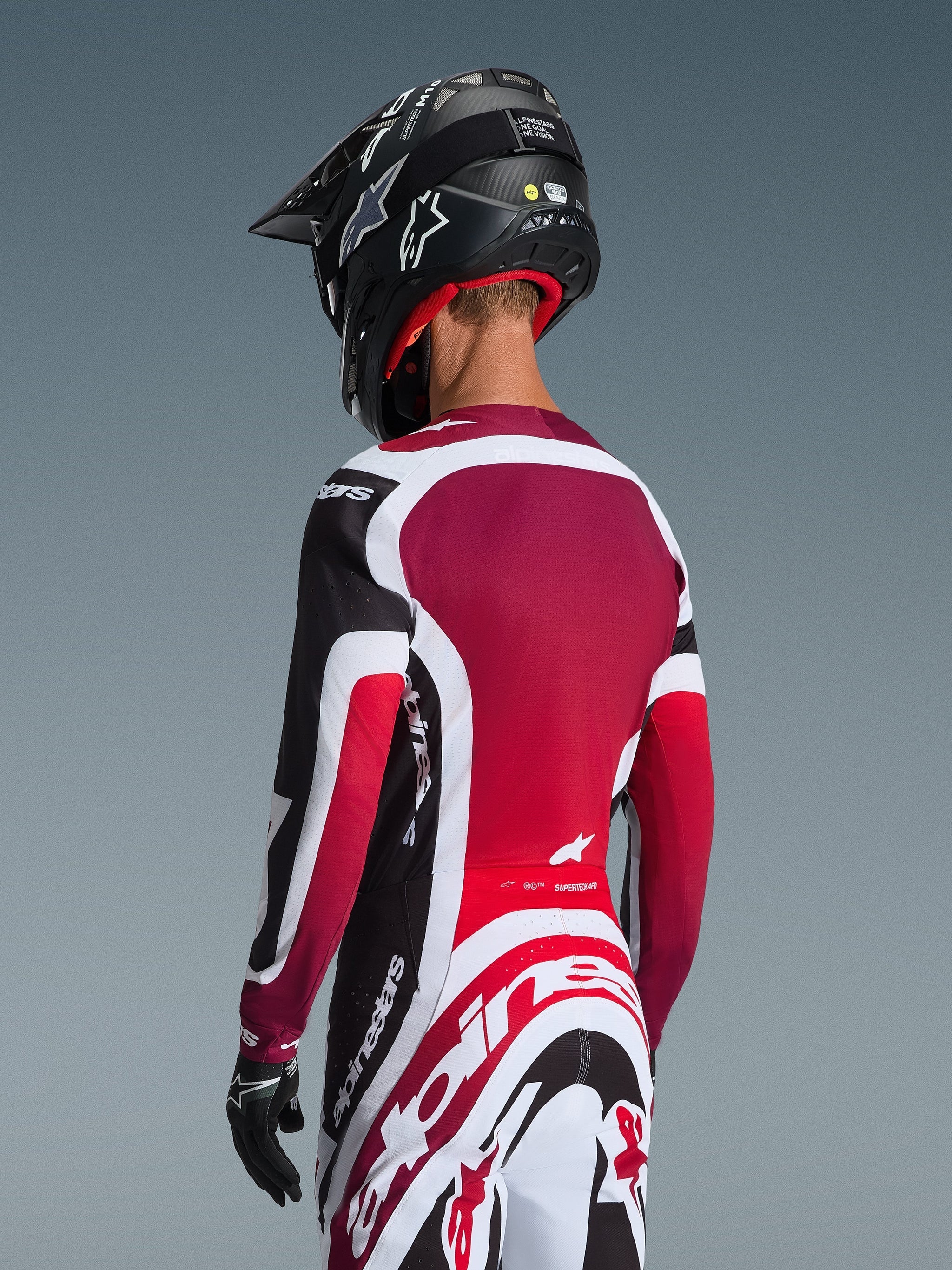 Achteraanzicht van een motocrossrijder die de 2026 Supertech AFD Vista Jersey draagt in zwart, rood en wit, gecombineerd met een bijpassende broek en een zwarte helm, voorzien van opvallende Alpinestars-branding, rode mesh-panelen en een atletische racepasvorm.