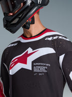 Alpinestars 2026 Supertech AFD Vista Jersey, Black Red and White, close-up of chest showing Alpinestars star logo and 'Supertech AFD' text, featuring laser-cut ventilation holes and mesh construction, worn with black motocross helmet.