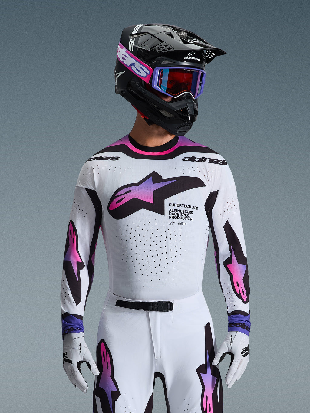 Alpinestars 2026 Supertech AFD Vista Gear Set, professional motocross racing gear, white jersey and pants with pink and purple gradient graphics, black helmet with purple goggles and white gloves, athletic race fit for off-road performance.