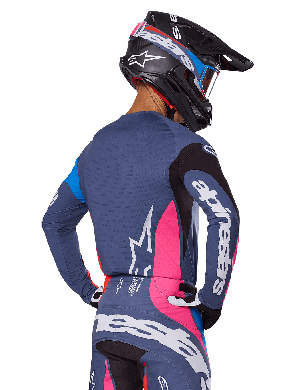 Motorcrosser van achteren gezien in de Alpinestars 2025 Techstar Dreem uitrustingsset in grijs, met een blauwgrijze jersey en broek met roze en zwarte panelen, witte Alpinestars-logo's op de mouwen en rug, en een bijpassende zwarte helm met blauwe en roze graphics.