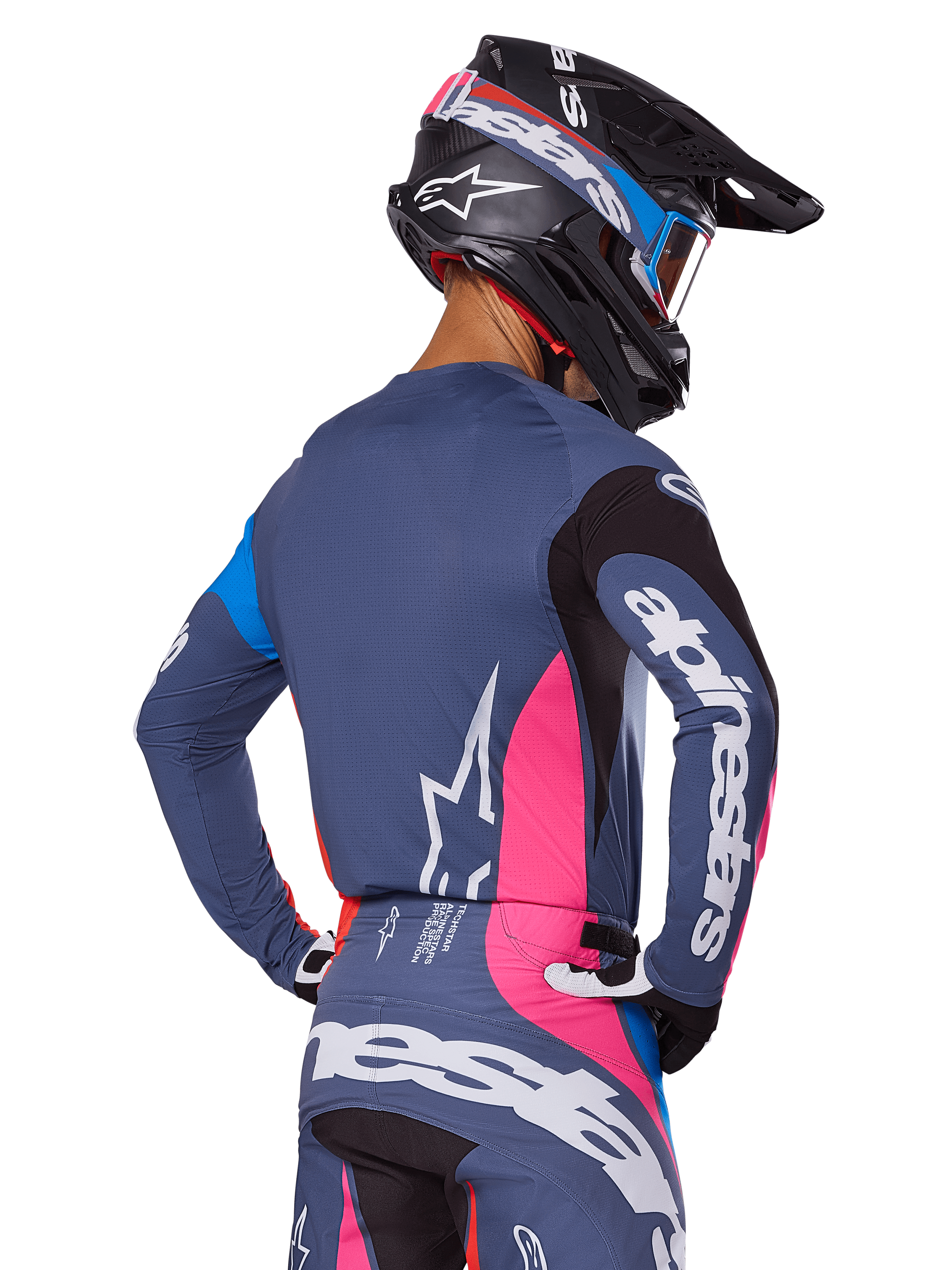 Motorcrosser van achteren gezien in de Alpinestars 2025 Techstar Dreem uitrustingsset in grijs, met een blauwgrijze jersey en broek met roze en zwarte panelen, witte Alpinestars-logo's op de mouwen en rug, en een bijpassende zwarte helm met blauwe en roze graphics.
