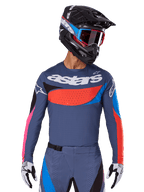 Alpinestars 2025 Techstar Dreem Jersey, motorcross jersey, grijs met blauwe, rode en roze accenten, voorzien van lasergesneden perforaties en groot logo op de borst, gedragen met bijpassende broek en zwarte racehelm
