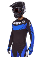 Motocrossrijder in de Alpinestars 2025 Techstar Dreem gearset, zwart shirt met blauwe geperforeerde panelen en witte logo's, bijpassende zwarte en blauwe broek, zwarte racehelm en blauwe handschoenen, gecoördineerde performance-outfit voor off-road motocross.