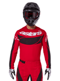Alpinestars 2025 Techstar Dreem Jersey, motorcrosskleding, helderrood en zwart, met een wit 'astars' logo en zwart geventileerd borstpaneel, gedragen met bijpassende broek, zwarte helm en zwart-witte handschoenen, ontworpen voor professionele off-road racing