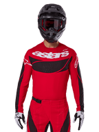 Alpinestars 2025 Techstar Dreem Jersey, motorcrosskleding, helderrood en zwart, met een wit 'astars' logo en zwart geventileerd borstpaneel, gedragen met bijpassende broek, zwarte helm en zwart-witte handschoenen, ontworpen voor professionele off-road racing