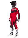Totaalbeeld van een motorcrossrijder in de 2025 Techstar Dreem Gear Set in felrood en zwart, bestaande uit een performance jersey met witte branding, bijpassende stretch ripstop broek, zwarte helm met rood vizier, wit-zwarte handschoenen en witte Tech-laarzen; een gespecialiseerde race-outfit voor off-road competities.