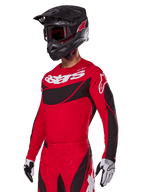 Alpinestars 2025 Techstar Dreem Gear Set, rode motorcross jersey en broek met zwarte en witte accenten, gedragen met een zwarte helm en crossbril, witte en zwarte handschoenen, voorzien van opvallende 'astars' branding, ontworpen voor prestatiegerichte off-road racing