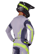 Motorcrosser van achteren in Alpinestars 2025 Techstar Dreem Gear Set, grijze jersey en broek met opvallende neongeel-groene branding, bijpassende zwarte helm met neon graphics, professionele motorcross outfit