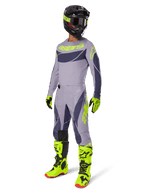 Alpinestars 2025 Techstar Dreem Gear Set, motorcrosser in volledige race-outfit, grijs shirt en broek met donkergrijze patronen en neon geelgroene accenten, bijpassende zwarte helm, neon geelgroene handschoenen en laarzen, hoogwaardige off-road uitrusting
