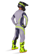 Motocrossrijder van achteren gezien in de Alpinestars 2025 Techstar Dreem Gear Set, grijs en donkergrijs met fluorescerend gele branding, bijpassende jersey en broek, zwarte helm met gele accenten en fel fluorescerend gele laarzen, gecoördineerde professionele motocross-race-outfit.