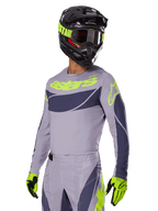 Motorcrossrijder in Alpinestars 2025 Techstar Dreem Jersey, grijs en donkergrijs met limegroene logo's, bijpassende broek, zwarte helm met limegroene accenten, limegroene en zwarte handschoenen, gecoördineerde outfit voor off-road racing