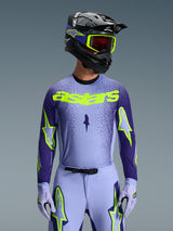 Alpinestars 2026 Supertech Scenz Jersey, motorcross jersey, paars en fluorgeel, gedragen door een rijder met een bijpassende zwart-paarse helm, neongele crossbril en paarse crossbroek, voorzien van neongeel astars-logo op de borst en sterlogo's op de mouwen.