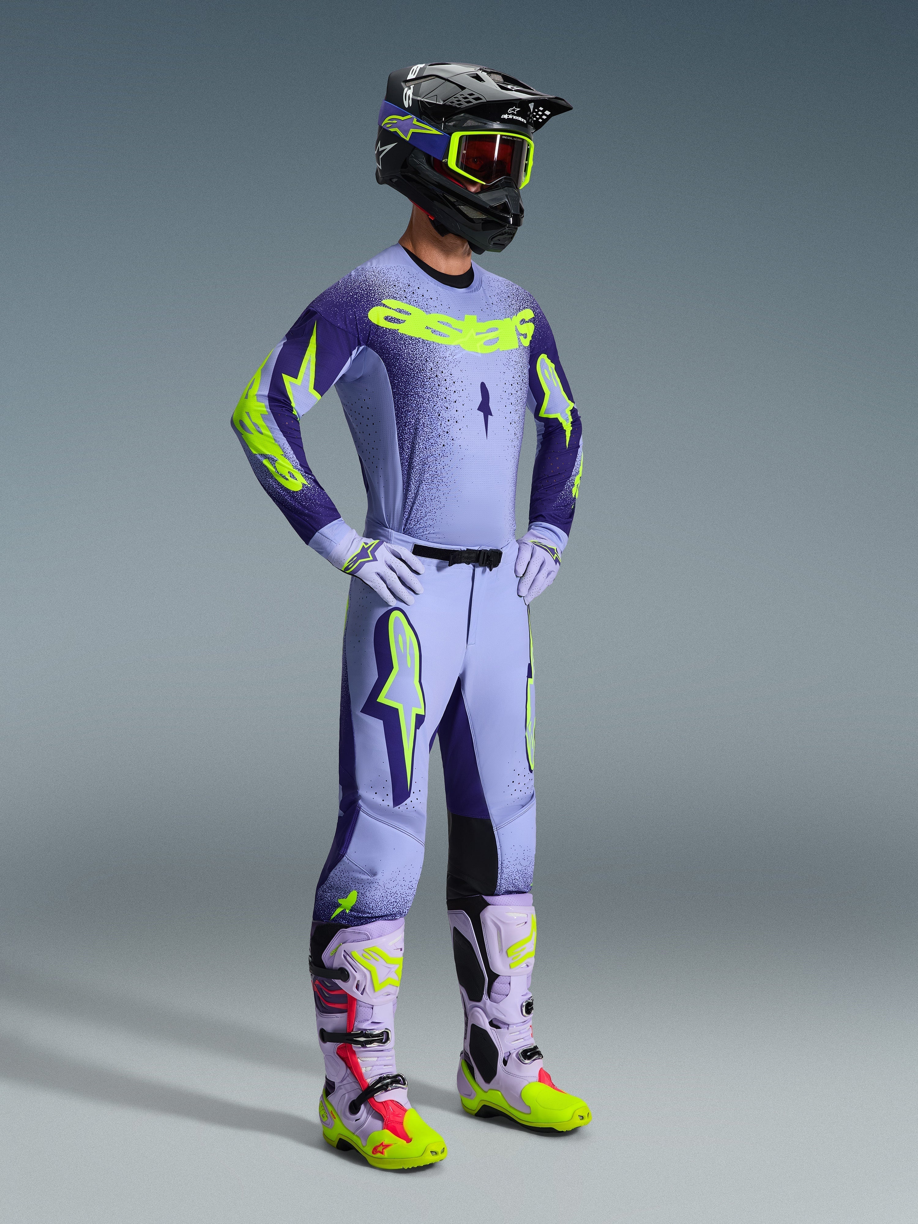 Motocross rider wearing the 2026 Supertech Scenz Jersey and full racing kit, Purple and Yellow Fluo design with light purple base and neon accents, matching pants with bold star logos, black helmet with neon yellow goggles, coordinated purple and neon yellow boots, professional off-road gear set.