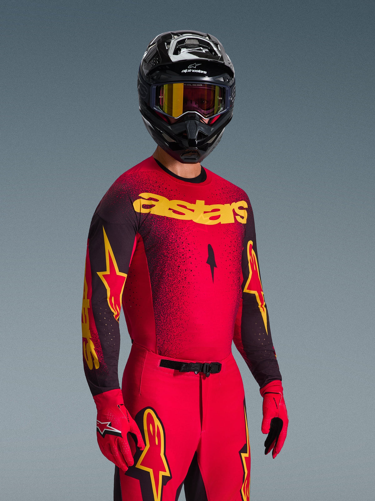 Motorcrosser in Alpinestars 2026 Supertech Scenz Jersey, rood en zwart met gele 'astars' branding, bijpassende rode broek en handschoenen, zwarte helm met crossbril, professionele race-uitrusting voor off-road motorcross