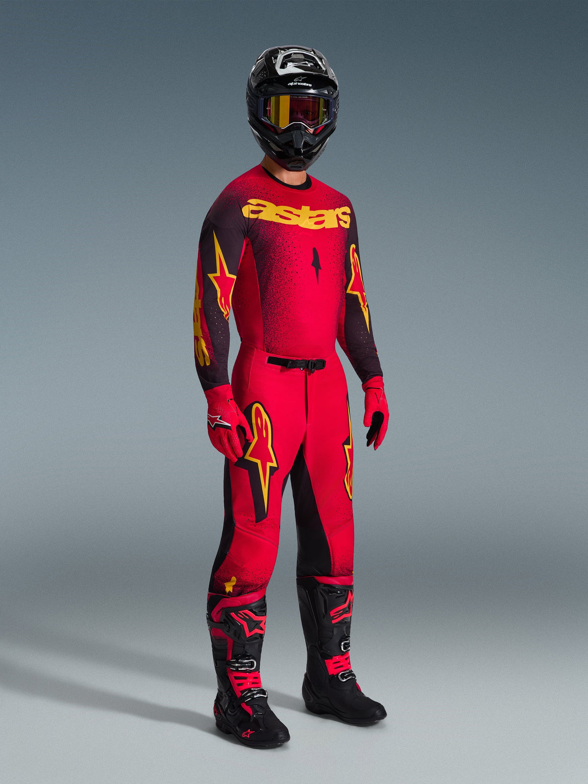 Motorcrosser met de Alpinestars 2026 Supertech Scenz jersey in rood, zwart en geel, bijpassende rode broek met zwarte en gele accenten, zwarte helm met crossbril, rode handschoenen en zwarte laarzen met rode details, complete professionele race-uitrusting set