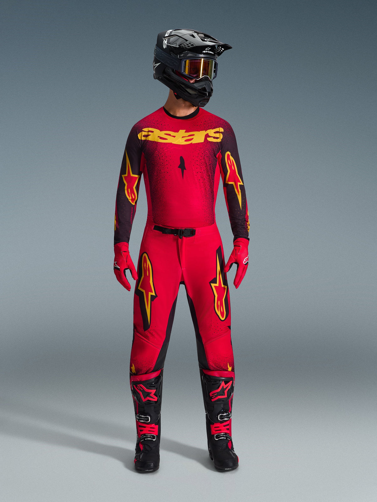 Motocrosser in de Alpinestars 2026 Supertech Scenz Jersey in Red Black Yellow, gecombineerd met bijpassende broek, zwarte helm met crossbril, rode handschoenen en zwart-rode laarzen, professionele race-uitrusting voor off-road prestaties