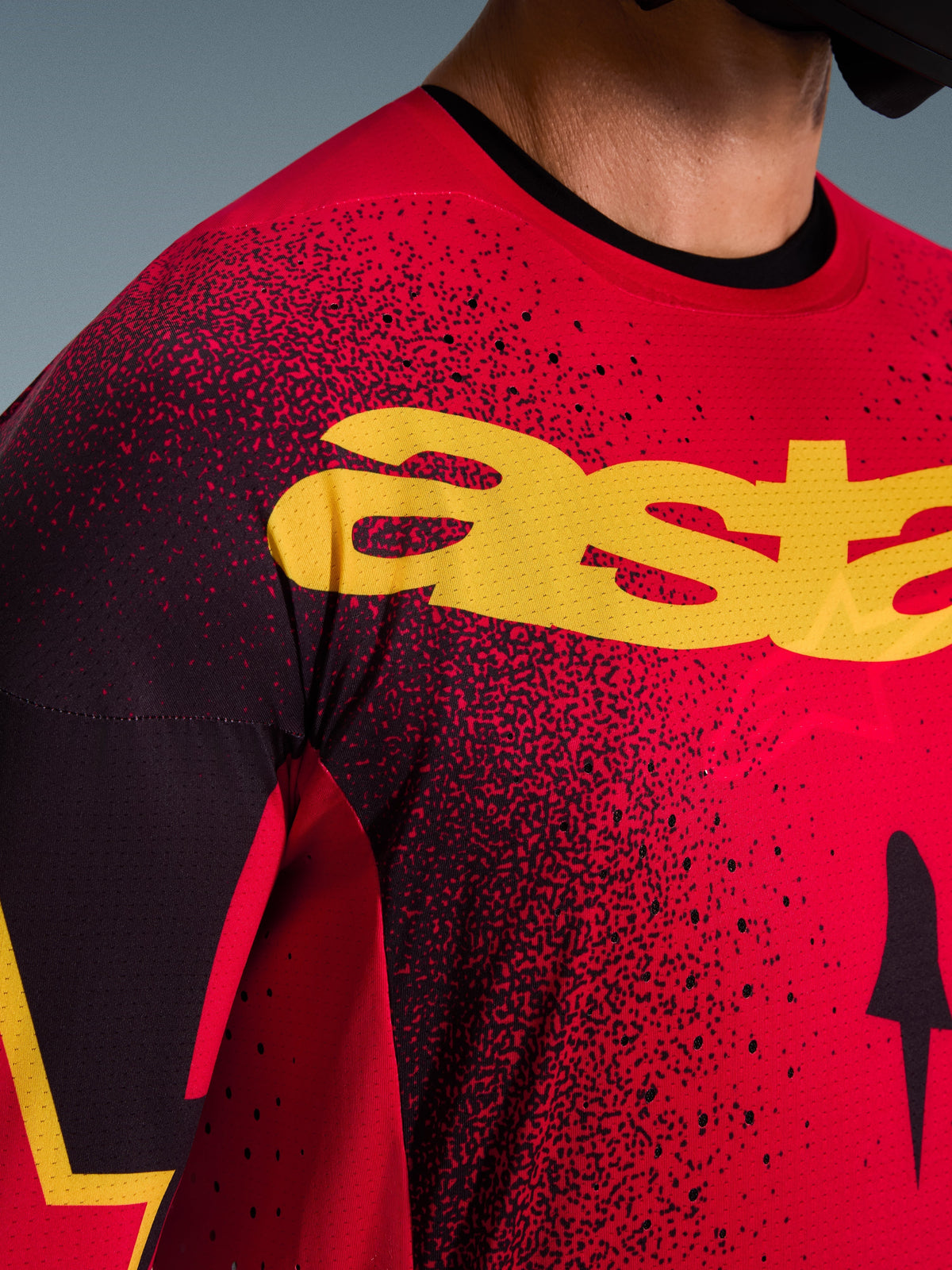 Alpinestars 2026 Supertech Scenz Jersey, motorcross jersey, rood, zwart en geel, close-up van de borst met gele branding, zwart gespikkeld patroon en laser-gesneden perforaties voor ventilatie.