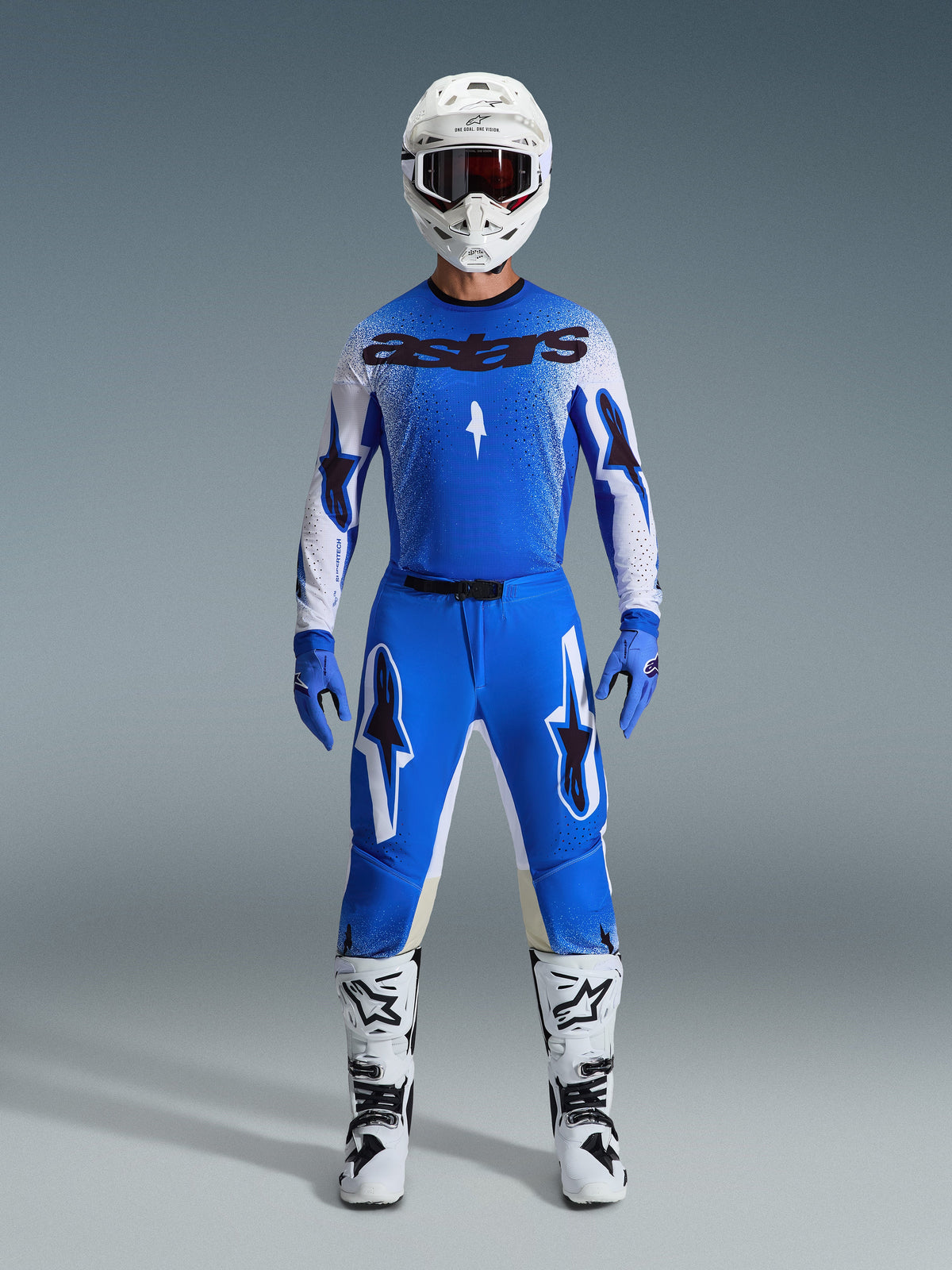 Motocross rider wearing the Alpinestars 2026 Supertech Scenz Gear Set in Ucla Blue and White, featuring a lightweight blue and white jersey with black branding, matching blue pants, white racing helmet, and white motocross boots, pro-level performance gear for off-road racing.