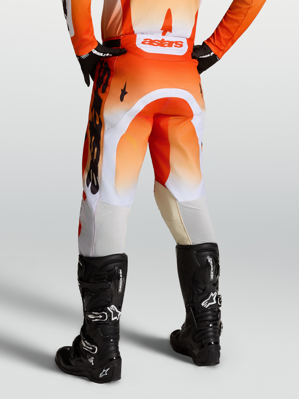 Alpinestars Racer Amber Broek voor heren, motorcrossbroek in oranje en wit met zwarte motorlaarzen, duurzame 600D polyfabric, off-road racing, achteraanzicht.