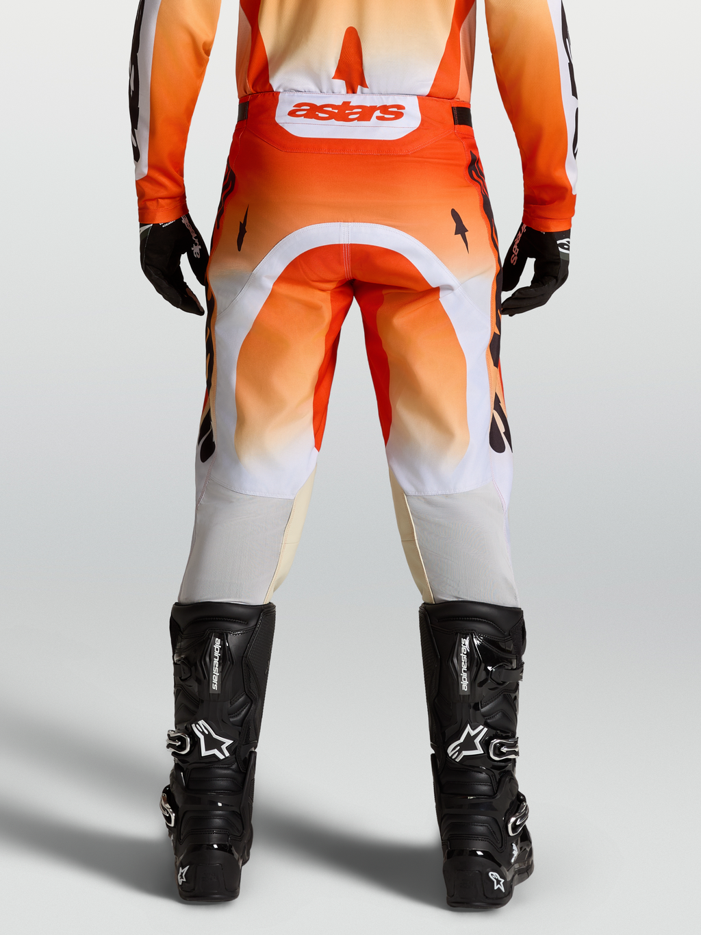 Alpinestars Racer Amber broek, motocrossbroek in rood en wit, achteraanzicht op model met zwarte motorlaarzen.